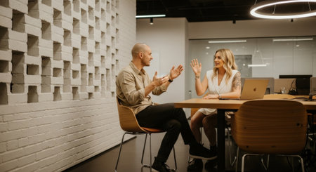 Two professionals collaborate at a table in a modern office, sharing ideas and working on a laptop, fostering teamwork and innovation.の素材