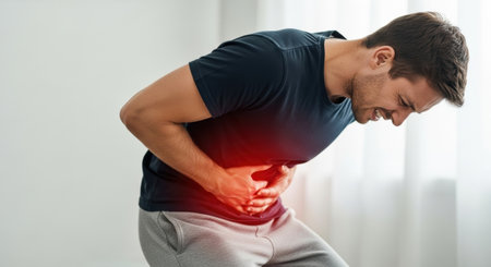 A man is shown doubled over in pain, clutching his stomach, indicating a possible medical issue or discomfort. The image highlights the physical manifestation of abdominal pain.の素材