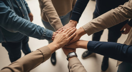 A group of people join hands in a gesture of teamwork, symbolizing unity, collaboration, and shared goals in a business or community setting.の素材