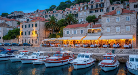 A picturesque harbor in a European coastal town at twilight, featuring docked boats and illuminated restaurants along the waterfront.の素材