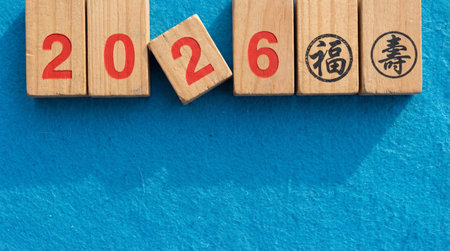 the image shows wooden blocks arranged to display the year two thousand twenty six with chinese symbols on a bright blue textured surfaceの素材