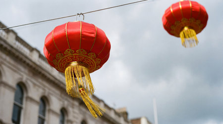 two red chinese lanterns hang outdoors against a cloudy sky, with a building visible in the background, adding a festive touch to the sceneの素材