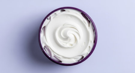 A top-down view of a small bowl filled with thick, creamy white yogurt, swirled into a decorative pattern, set against a light purple background.の素材