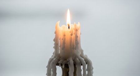 A detailed shot of a lit candle, showcasing the warm glow of the flame and the textured, solidified wax that has dripped and accumulated along its sides, set against a soft, out-of-focus backdrop.の素材