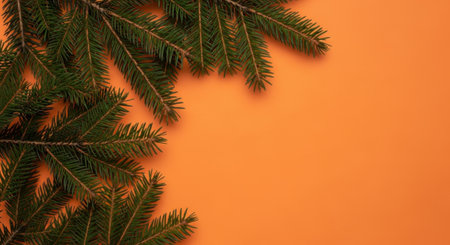Close-up of fresh green fir branches on a vibrant orange background, perfect for holiday designs.の素材