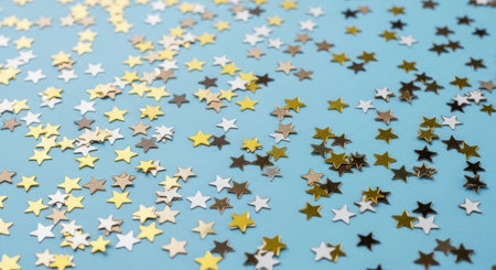 A cheerful scattering of gold and silver star confetti on a light blue surface, perfect for adding sparkle to any celebration.の素材