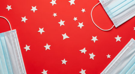 Three light blue medical face masks are arranged on a bright red background, interspersed with numerous small white star-shaped confetti. The composition suggests a blend of health precautions and festive or patriotic themes, creating a visually striking and meaningful image.の素材