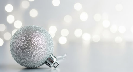 A close-up shot of a silver Christmas ornament on a white surface, with a blurred bokeh background of lights.の素材