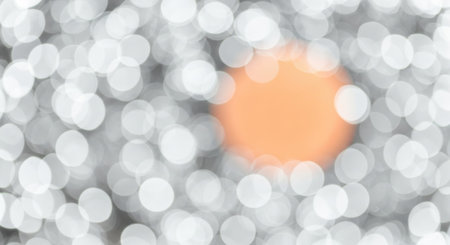 An abstract bokeh background featuring a prominent orange highlight amidst a sea of blurred white and gray circles, creating a festive and dreamy atmosphere.の素材