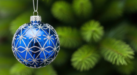 A close-up shot of a blue Christmas ornament with white detailing hanging on a green tree branch, creating a festive holiday scene.の素材