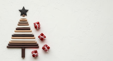 A festive Christmas tree made of chocolate sticks with a star on top and small gift boxes around it, set against a white background.の素材