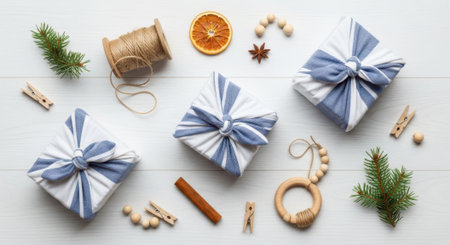 Overhead view of three Christmas gifts wrapped in blue and white striped fabric, accompanied by natural decorations like dried orange slices, cinnamon sticks, pine branches, and wooden ornaments, all arranged on a white wooden background.の素材