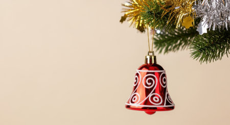 A close-up of a red Christmas bell ornament with white swirls, hanging from a decorated tree branch with gold and silver tinsel.の素材