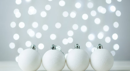 Four white Christmas ornaments in a row with bokeh lights in the background, creating a festive atmosphere.の素材