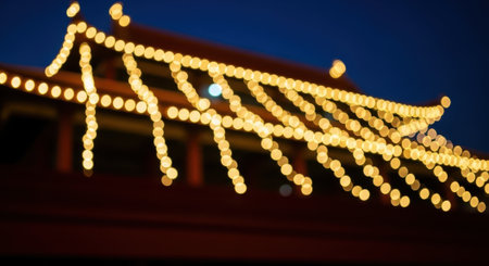 A close-up view of a traditional Asian roof structure adorned with glowing yellow string lights against a dark blue twilight sky.の素材