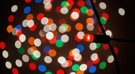 A festive and colorful display of out-of-focus Christmas lights creates a beautiful bokeh effect, with one individual red light bulb sharply in focus against the blurred background.の素材