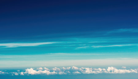 An aerial view of a deep blue sky with thin, horizontal clouds stretching across the horizon, above a layer of fluffy white clouds.の素材