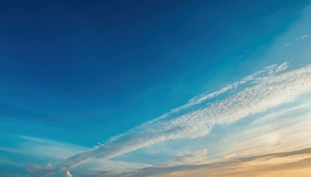 A breathtaking view of a clear blue sky with delicate white clouds stretching across, meeting a warm golden horizon.の素材