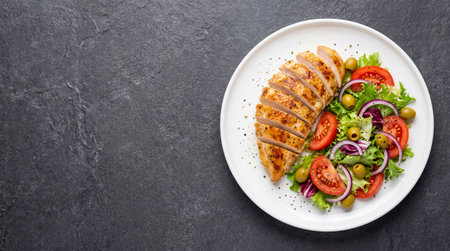 A delicious and healthy meal featuring perfectly grilled chicken breast served alongside a vibrant salad of fresh tomatoes, olives, red onions, and lettuce.の素材