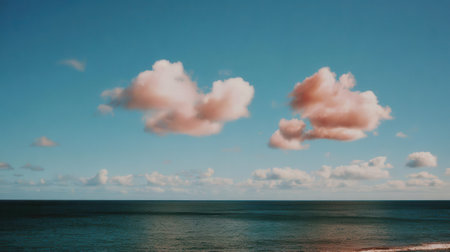 A serene seascape featuring fluffy pink clouds drifting across a vast blue sky, with the calm ocean stretching to the horizon.の素材