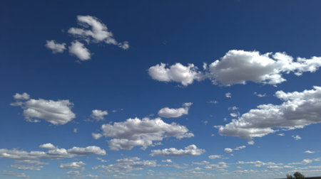 A beautiful expanse of clear blue sky dotted with scattered, puffy white cumulus clouds, suggesting fair weather and a bright day.の素材