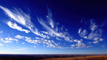 A panoramic view of a deep blue sky filled with delicate, wispy clouds stretching across the horizon above a dry, brown landscape.の素材