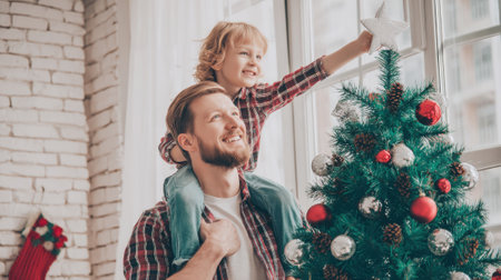A father carries his son on his shoulders as they decorate a Christmas tree, creating a festive holiday atmosphere.の素材