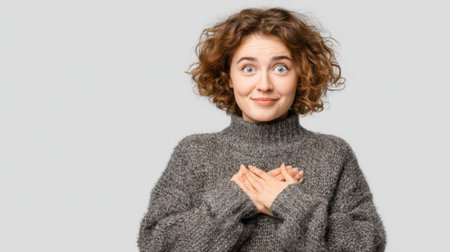 a woman with curly hair wearing a gray sweater and hands crossed over her chest smiles at the camera in a studio shot against a plain backgroundの素材