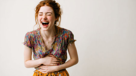 a young woman with red hair is laughing heartily with her hands on her stomach, wearing a colorful floral shirt and patterned skirt against a light backdropの素材