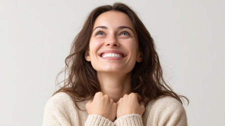 a woman with brown hair is smiling and looking upwards with her hands near her chest area, conveying a sense of happiness and positivityの素材