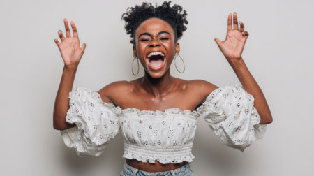 a woman with curly hair is ecstatically raising her hands, wearing a white floral top and hoop earrings, against a plain backdrop, radiating joyの素材