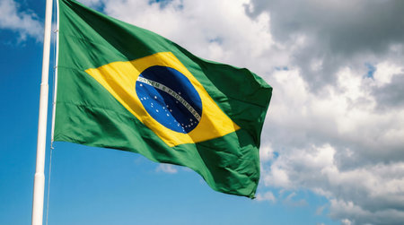 a Brazilian flag waves proudly in the wind, set against a beautiful sky filled with fluffy clouds, symbolizing national pride and identityの素材