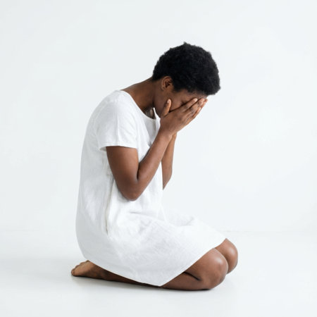 a woman in a white dress is kneeling with her hands covering her face, expressing sadness and despair.の素材