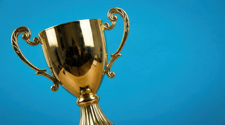 Close-up shot of a shiny gold trophy cup, set against a vibrant blue backdrop, representing victory and accomplishment.の素材