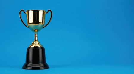 A shiny golden trophy stands prominently against a vibrant blue backdrop, representing victory and accomplishment.の素材