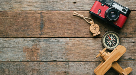Overhead shot of travel-related items, including a camera, compass, and airplane model, arranged on a weathered wooden surface, evoking a sense of exploration and journey.の素材