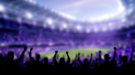 A silhouetted crowd of excited fans with their hands in the air at a brightly lit stadium, cheering for their team during a sports match.の素材