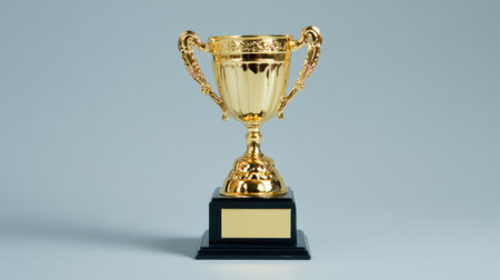 A shiny golden trophy with handles and a black base sits on a plain grey background.の素材