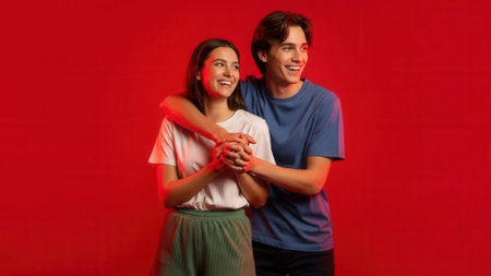 A joyful young couple, a man and a woman, share a happy moment, embracing and smiling warmly. They are set against a striking, solid red backdrop, creating a visually engaging and positive atmosphere.の素材