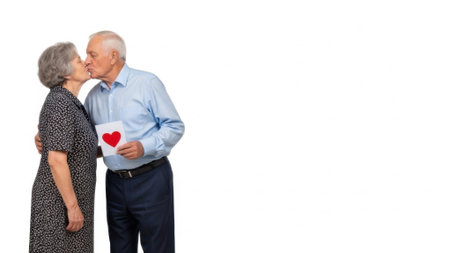 An elderly couple shares a tender moment, the man holding a Valentines card with a red heart, on a white background.の素材