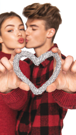A young couple shares a playful kiss while holding a sparkling heart-shaped decoration, symbolizing their romantic bond and affection. Perfect for Valentine's Day.の素材