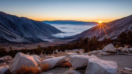 A breathtaking view of the sun rising over a mountain range, casting a golden glow. A thick blanket of fog rests in the valley below, creating a stunning inversion.の素材