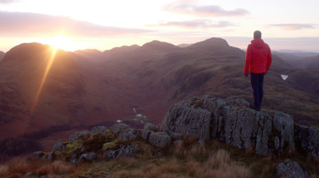 A lone hiker stands on a rocky summit, watching the sun rise over a vast, rugged landscape, evoking a sense of peace, freedom, and adventure.の素材