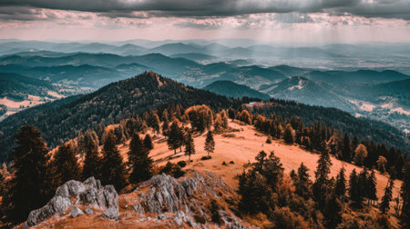 Breathtaking panoramic shot of rolling hills and a prominent mountain summit covered in trees. The moody, cloudy sky creates an epic and atmospheric natural landscape scene.の素材