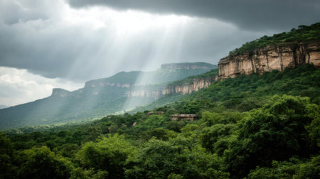 A breathtaking view of a verdant mountain range under a dramatic, cloudy sky. Rays of sunlight shine down through the clouds, highlighting the lush forest and rocky cliffs.の素材