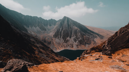 A stunning view from a high vantage point, looking down at a serene lake surrounded by towering, rugged mountain peaks under a cloudy sky.の素材