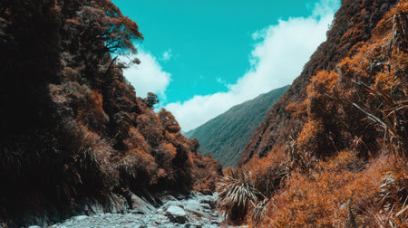 A stylized nature scene of a stream in a mountain gorge. The contrasting colors of the teal sky and rust colored plants create a dramatic and beautiful landscape.の素材