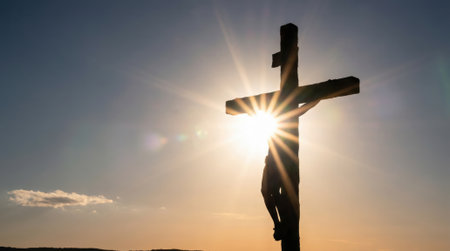 A powerful silhouette of the crucifixion of Jesus Christ on a wooden cross against a dramatic sunset sky. The sun creates a brilliant starburst behind the figure.の素材
