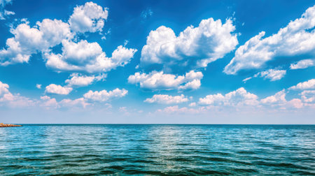 A stunning panoramic view of the ocean on a sunny day. The water is calm and clear, reflecting the bright blue sky filled with beautiful white puffy clouds.の素材
