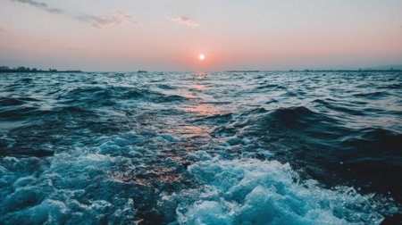 A breathtaking view of the ocean at dusk. The sun sets on the horizon, its light reflecting on the deep blue, choppy waves, creating a tranquil yet powerful natural scene.の素材